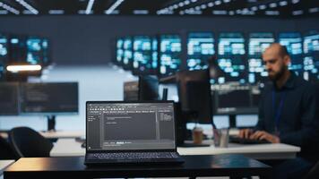 Focus on laptop used by programmer running code in blurry background for data center servers, troubleshooting rigs. Close up shot of code lines on notebook screen in server hub photo
