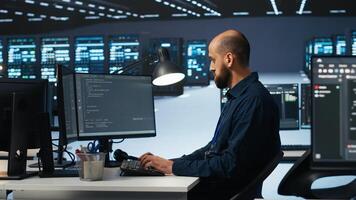 IT engineer programming in server hub housing advanced equipment storing massive datasets. Technician typing code on computer to mend data center racks doing complex computational operations photo