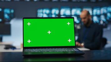 Focus on green screen laptop in server room used by man in blurry background to safeguard data from threats. Close up shot of chroma key notebook used by specialist protecting supercomputers photo