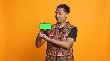 Content creator in traditional clothing recommending isolated screen phone, studio backdrop. Indian man reviewing copy space mockup smartphone device for online tech channel, camera B photo