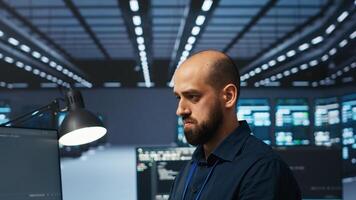 Programmer writing code, working in network security data center facility, ensuring optimal performance. IT specialist using PC to monitor energy consumption across operational server racks photo