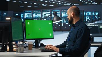 Man typing code on green screen computer in high tech data center with server rows providing computing resources. IT specialist using mockup PC to oversee rackmounts operating data photo