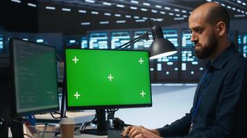 System administrator working on green screen computers in data center, ensuring optimal performance. Worker monitoring energy consumption across servers with mockup PC displays photo