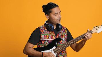 Happy man holding electric guitar, playing rock music, isolated over studio background. Cheerful indian musician using musical instrument, doing concert, playing songs, camera A photo