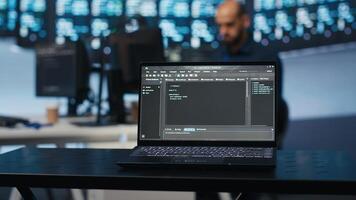 Focus on laptop used by technician in blurry background programming in data center room housing servers. Close up shot of code lines on notebook display in data storage facility photo