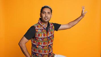 Radiant person having fun, dancing on oriental music, enjoying relaxation time. Joyous man doing entertaining bollywood dance moves, isolated over studio background, camera B photo