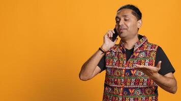 Man discussing with best friend over telephone call, enjoying leisure time. Upbeat person wearing indian attire talking with mate in phone call, isolated over studio backdrop, camera A photo