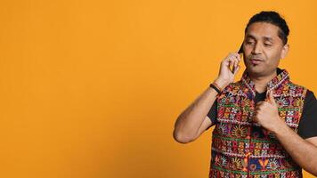 Happy man in traditional clothing chatting with best friend over telephone call. Upbeat person with colorful attire communicating with mate using phone, studio background, camera B photo