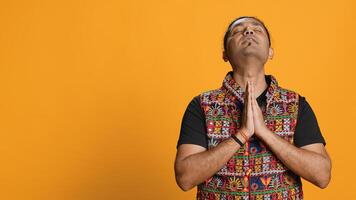 Pious indian man praying to his god, asking for forgiveness. Spiritual person doing worship hand gesturing, confessing, begging for pardon, isolated over studio background, camera A photo