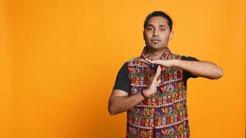 Portrait of assertive indian man asking for timeout, doing hand gestures, feeling fatigued. Firm person doing vehement pause sign gesturing, wishing for break, studio background, camera B photo