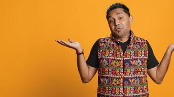 Indian man shrugging shoulders, unable to provide answer, having detached apathy facial expression. Apathetic person doing hand gesturing showing lack of knowledge, studio background, camera A photo