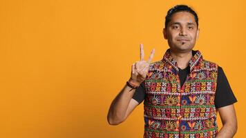 Portrait of upbeat man crossing fingers to make wish, hoping for good luck, isolated over studio background. Jolly indian person doing peace victory hand sign gesture, camera A photo