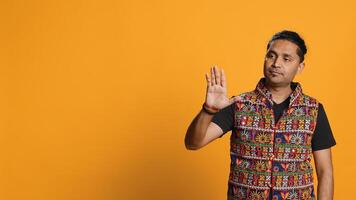 Indian man trying to stop chaotic fight using calming hand gesture to diffuse tensions, doing peaceful resolution. Reassuring person doing calm down sign gesturing, studio background, camera A photo