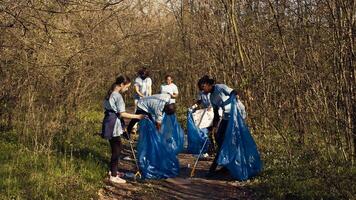 Group of volunteers working to clean the forest from garbage, collecting trash and plastic waste in bags. Environmental activists grabbing rubbish and recycling, support ecological justice. Camera B. photo