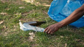 People supporting cleanup of the natural environment by grabbing recyclables and trash objects from the woods, collecting in a garbage bag. Using utensils to pick up rubbish. Close up. Camera A. photo