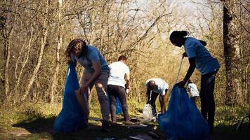 Team of volunteers collecting rubbish to fix pollution problem within the habitat, protect the natural environment. Activists doing voluntary work to clean the woods from trash. Camera B. photo