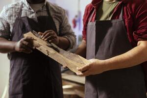 Manufacturer and apprentice selecting high quality wood materials, ensuring they align with project requirements. Cabinetmaker and colleague doing quality assurance on lumber piece, close up shot photo