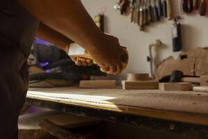 Woodworker at workbench using manual sandpaper to sander timber block, assembling furniture in joinery. Carpenter smoothing piece of wood, spreading sawdust everywhere, close up shot photo