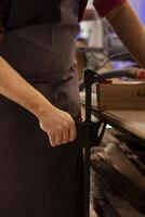 Artisan using bench vise to hold lumber block, starting designing wood art in studio, close up shot. Woodworking specialist in carpentry shop using sash clamp to secure piece of wood tightly photo