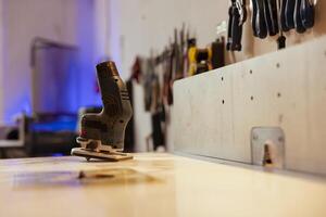 Close up shot of electric router on workbench in assembly shop with woodworking tools on rack in background. Focus on hand powered gear used for cutting wood in carpentry studio photo