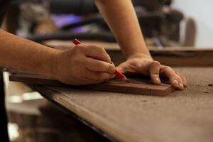 Artisan using ruler to take measurements of plank used to make creative wood sculptures in studio. Man drawing with pencil on wooden board to accurately determine where to make cut, close up shot photo