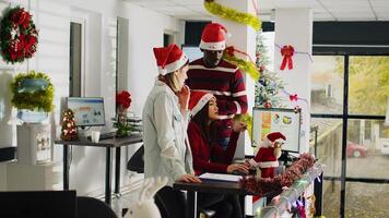 Employees gathered together at computer desk brainstorming ideas for project in Christmas decorated office. Diverse group of workers in multicultural workplace adorn with xmas lights and garlands photo
