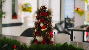 Dolly in close up shot on mini Christmas pine tree decoration placed in empty office. Festive workplace filled with xmas lights, garlands and wreaths during winter holiday season photo