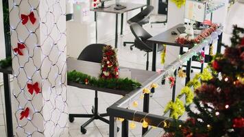 Zoom in on beautifully decorated Christmas pine tree placed in empty office. Xmas tree adorn with red bows and baubles in festive workplace filled with lights during winter holiday season photo