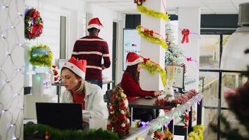 African american staff member working during Christmas season in festive decorated office, showing supervisor task progress. Multiethnic diverse team in xmas ornate workplace during holiday season photo