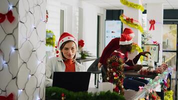 Happy multiethnic team working on christmas season in decorated office. Cheerful employees solving tasks at desk in diverse workplace next to colleagues during winter festive time photo