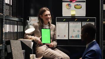 Female inspector speaking with policeman while vertically holding digital tablet with isolated chromakey mockup template. Multiethnic investigators utilizing smart device with greenscreen display. photo