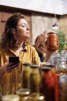 Healthy living woman in zero waste store using smartphone notes app to check shopping list. Meticulous customer looking to replenish pantry at home with natural pesticides free food essentials photo