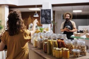 Customer inquiring about natural pesticides free products in zero waste shop, with vendor happy to help. Ecofriendly supermarket client in need of organic natural food, being helped by friendly seller photo