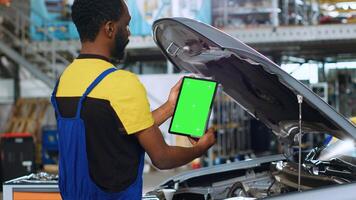 Trained repairman using green screen tablet in car service to order new parts for busted vehicle. Repair shop employee using chroma key device to look online for replacing components photo