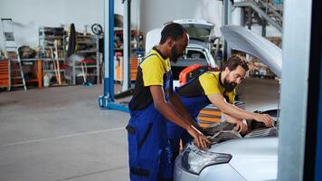 Trained technicians in auto repair shop working together on fixing car, discussing best options. Professional and colleague collaborating on servicing broken vehicle, checking for defective components photo
