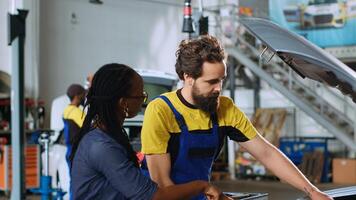Qualified serviceman in repair shop showing client damages found inside car after inspection. Automobile specialist telling woman vehicle diagnostic after checking for defective parts photo