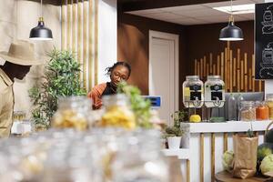 At the checkout desk, a young black woman is taking goods out of the basket for weighing. African American female cashier being of service to the male customer at the counter. photo