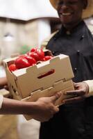 A smiling black man in a modern store offers fresh local produce, reusable containers, and bulk options for an eco-conscious lifestyle. Close-up shot of vendor receiving crates of products. photo