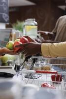 The close-up shows two African Americans' hands carrying a bunch of apples above the checkout counter. The image focused on a male customer giving fruits to the black vendor for weighing. photo