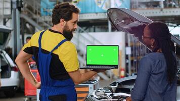 Trained serviceman using green screen laptop in car service to show customer parts needed for busted vehicle. Repair shop worker using chroma key device to search online for auto components photo