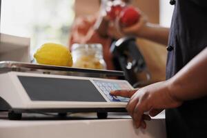 Close-up shot of a pair of African American hands holding red apples over the checkout counter. Selective focus on a female vendor weighing locally grown lemon on a scale. photo