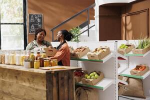 African American vendor sells fresh, organic fruits and vegetables at green grocery store. Local farmer giving crates of freshly harvested organic produce to female shopkeeper. photo