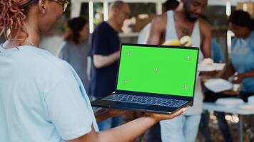 Detailed view of african american female volunteer holding laptop with isolated copyspace display for customization. Black lady holds minicomputer with green screen chromakey template in her hands. photo