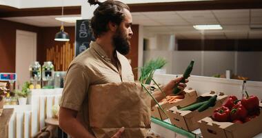 Man in zero waste shop buying vegetables, checking products before making purchase decision to ensure they are pesticides free. Vegan client verifying food in local store is organic, smelling it photo