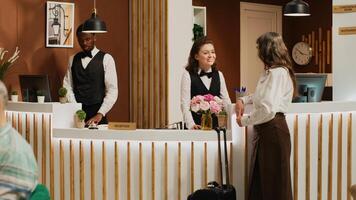 Female client checking in at luxury hotel lobby with assistance from friendly concierge staff. Receptionist greeting senior woman at front desk and helping with registration. Handheld shot. photo