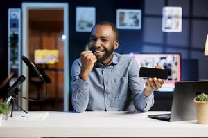 Excited BIPOC gamer playing games on livestream with fans watching, using powerful gaming smartphone. Streamer using mobile phone device to play videogames requested by subscribers photo