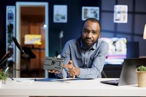 Man assessing V mount battery, expressing dissatisfaction with subpar quality. Content creator shooting review for online channel, displeased with rechargeable accumulator device performance photo