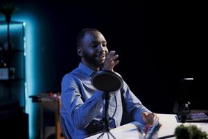 Entertaining streamer doing live broadcast in dark studio at night, talking to audience about daily activities. Celebrity gamer chatting with viewers, presenting game informations photo