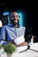 Cheerful content creator filming technology review of newly launched digital device, unboxing it and presenting specifications to audience. Internet star laughing while showing product to viewers photo