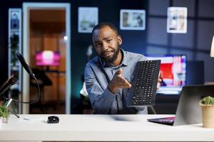 Content creator holding mechanical keyboard in hand, showing subscribers complete list of features and giving impressions on it. Tech expert showcasing computer peripheral to niche audience photo